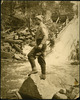 Original title:  Tom Thomson, standing on a rock fishing in moving water. 