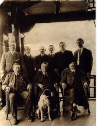 Original title:  Photograph shows Dr. Charles Edward Doherty, Medical Superintendent of Woodlands (back row 2nd from right) and other men and dog. The man at back row left appears to be T.S. Annandale. New Westminster Archives.